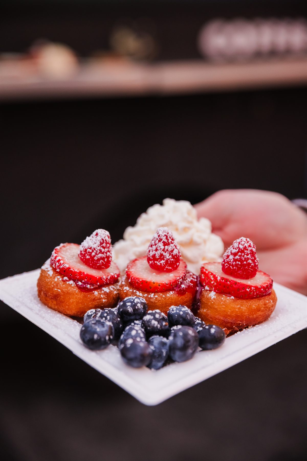 Three donuts on a plate, topped with sliced strawberries and whipped cream, with blueberries alongside.
