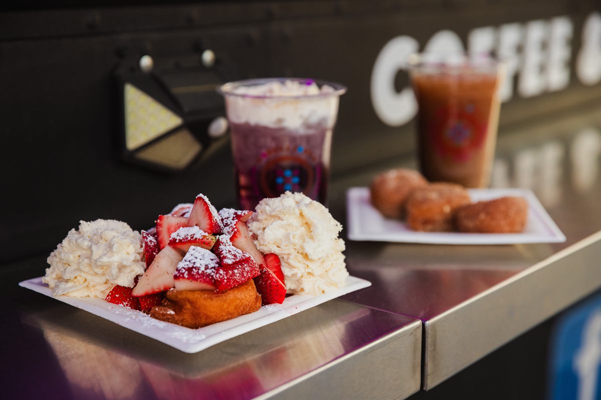 Donuts topped with sliced strawberries and whipped cream, and two cold drinks, on the truck’s counter.