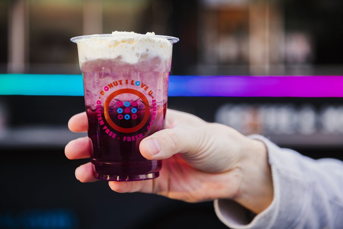 A hand holding a berry-coloured cream soda in a Donut I Love U cup, in front of the truck.